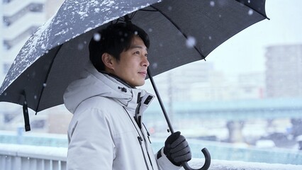 傘を差し雪の中を歩くコート姿の日本人男性