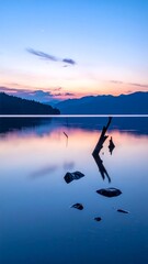 Serene landscape with tranquil water reflecting the colorful twilight sky, silhouetted mountains, and a few rocky outcroppings