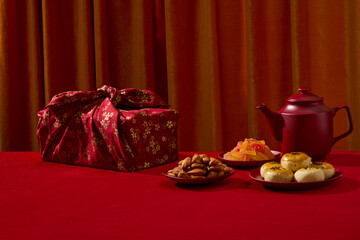 A Chinese New Year table scene with traditional cakes, tea, red gift box and decorative elements. Composition clean and commercial-friendly with space for design, front view