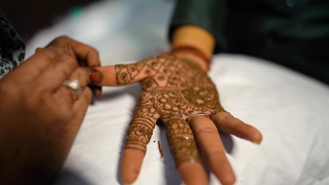 A mehndi artist applying detailed henna designs on the groom&rsquo;s hand during a traditional Indian wedding ceremony.
