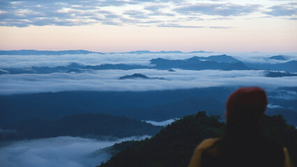 Blurred rear view of a woman sitting and looking at a beautiful foggy mountain before sunrise