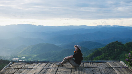 A woman sitting on wooden terrace and looking at a mountain view before sunset