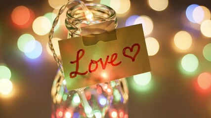 A glass jar with a love note and fairy lights inside on a colorful bokeh background