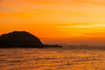 Golden sunset over tranquil coastal waters, silhouetted hills and glowing sky&mdash;perfect for travel ads, nature wallpapers, or screensavers. Serene, scenic, tropical, romantic escape.