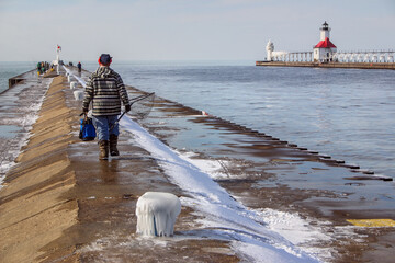 Fisherman walking down the south pier at St Joseph Michigan in winter to fish for Rainbow Trout