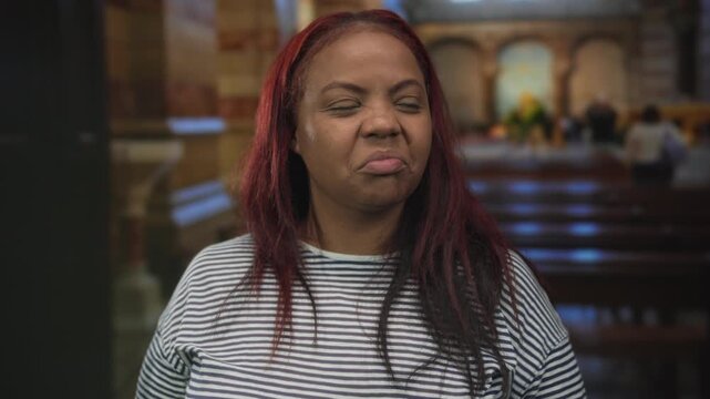Woman showing thumbs up in a historic church interior with wooden pews stained glass windows and brick columns; approval.