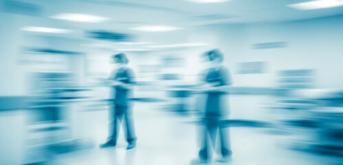 Blurry medical staff moving quickly in a bright blue toned room, expressing urgency and teamwork inside a modern hospital setting with motion blur and clinical lighting.