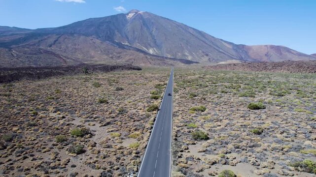Straight road leading toward Teide Volcano, with a car passing through volcanic terrain in Tenerife, Spain, suitable for travel and destination establishing shots.