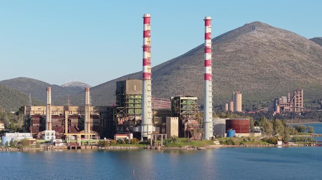 A drone orbits the Aliveri Power Station along the Evia coastline, revealing its industrial scale and dramatic seaside setting.