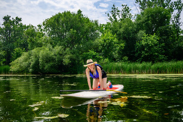 Adult beginner kneeling on a stand up paddle board in lagoon waters at the Toronto Islands, Canada, during summer. Introductory posture used for stability and confidence on calm freshwater.