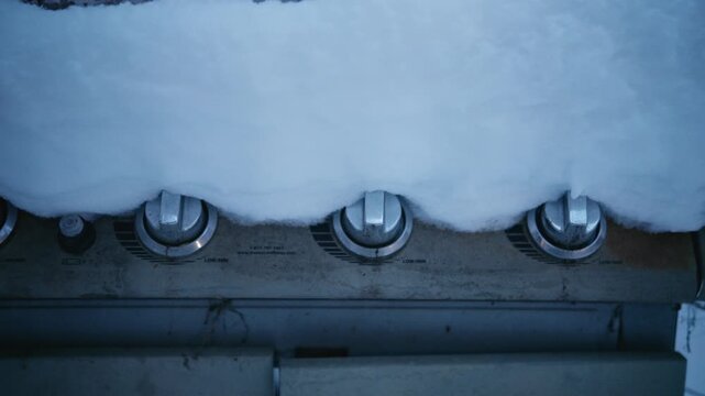 Fresh first snow blankets a backyard barbecue grill, signaling seasonal change and winter onset in a quiet residential yard. Lateral movement.