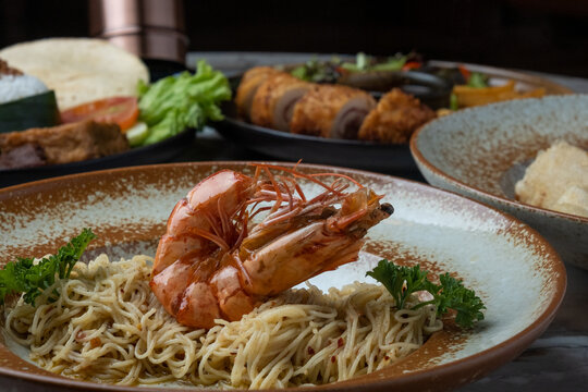 Close up photography of shrimp on aglio olio pasta, with various dishes on the background.