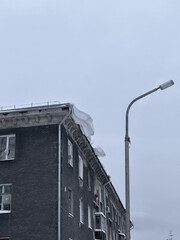 The facade of a gray building on a cloudy day, a block of snow hanging from the eaves.