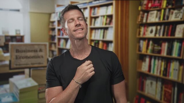 Man hand on chin in library aisle among densely packed bookshelves, looking upward at wooden shelves and book titles; thoughtful curiosity.