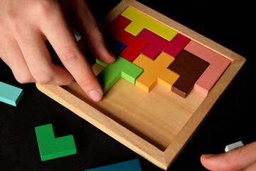 Close-up of hands solving wooden puzzle game on black background, logical thinking and mental health concept
