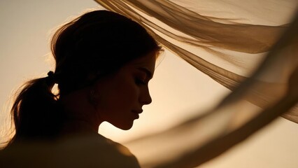 Silhouette of a woman in profile at sunset, hair in a ponytail, with soft flowing fabric in the background. Concept Sunset silhouette, Profile backlight, Flowing fabric, Ponytail silhouette