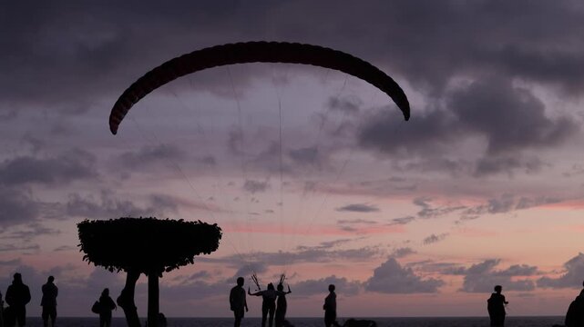 Silhouette of a paraglider preparing to launch against a vibrant sunset sky over the ocean in Turkey.