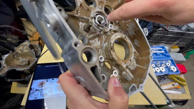 Close-up of mechanic checking alignment of the first bearing installed in the right half of scooter crankcase on a workbench, with tools visible during DIY maintenance