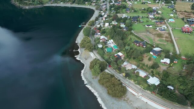 Tilting down drone aerial of Ranco Lake shoreline with coastal village, colorful houses, beach, and rural Chilean countryside landscape