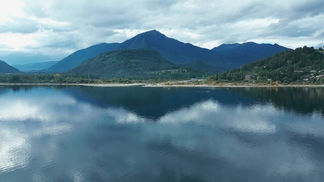 Panning drone aerial of Ranco Lake with mirror cloud reflections, mountains backdrop, beach shoreline, and serene Chilean panorama