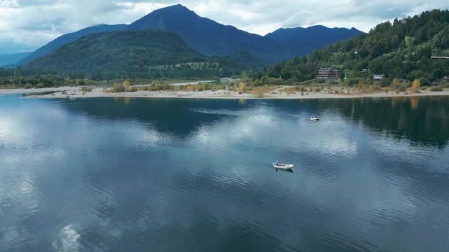 Backward drone aerial of boats on Ranco Lake with mountains backdrop, beach shoreline, autumn foliage, and serene Chile panorama