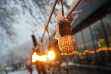 A frozen, burnt-out light bulb. Street lighting. Snowfall.