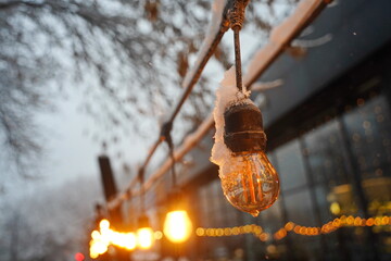 A frozen, burnt-out light bulb. Street lighting. Snowfall.