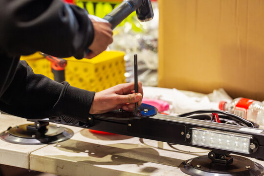 Male technician hammering a metal rod to make holes into a circular metal plate for light bar
