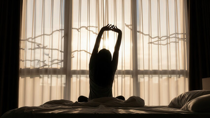 Woman stretching on a hotel bed in the soft morning light, silhouetted against large windows with sheer curtains, creating a tranquil and serene atmosphere