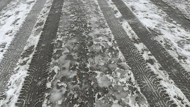 Tire tracks imprinted in a slushy, icy road surface with patches of melting snow, indicating winter driving conditions
