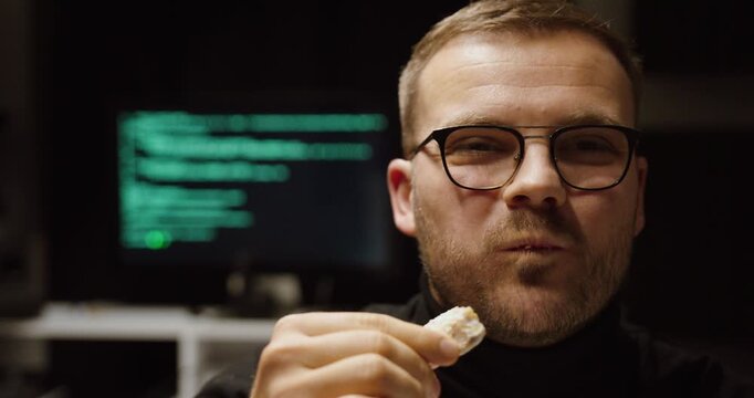Cinematic shot of a man eating while a blurred computer screen runs code behind him&mdash;concept for AI doing the work, automation, passive productivity, and time savings.