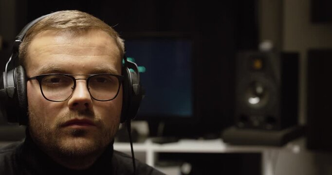 Cinematic portrait of a man in headphones in a home studio with a blurred computer screen behind&mdash;concept for AI music production, sound design, audio editing, and modern creative workflow.