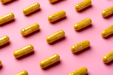 Yellow turmeric capsules create neat diagonal pattern on pink background, clean minimal concept for vitamin branding design.