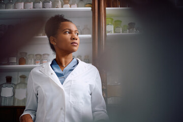 Portrait of pensive black pharmacist in pharmacy looking away.