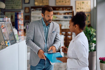 Mid adult man communicating with black female pharmacist in pharmacy.