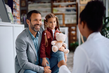 Happy father and daughter talking to pharmacist in pharmacy,
