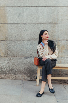 Thoughtful woman in casual outfit sitting on bench outdoors in Madrid