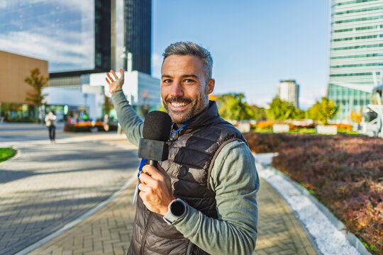 Reporter smiling outdoors with microphone in urban setting during autumn