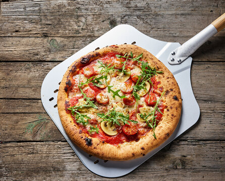 Naples style pizza with tomato mushroom and arugula on rustic wooden table
