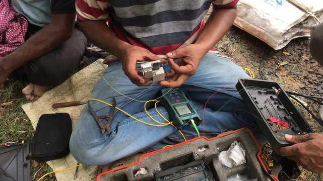 Close-up of an Indian male technician performing fiber optic fusion splicing using a splice machine to connect internet cables, showcasing telecom network installation and high-speed data infrastructu