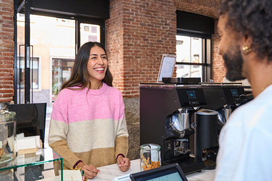 Smiling customer talking with barista at cafe counter during daytime