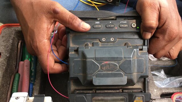 Close-up of an Indian male technician performing fiber optic fusion splicing using a splice machine to connect internet cables, showcasing telecom network installation and high-speed data infrastructu