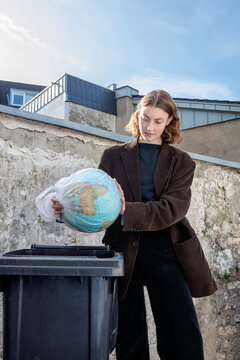 Teenage girl discarding globe in trash bin symbolizing environmental protection
