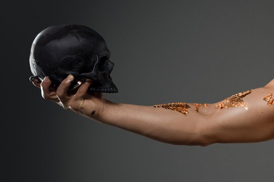 Individual holding a black skull in one hand with gold leaf on the arm in a studio setting during a creative session