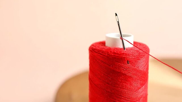 Close-up of a red spool with thread through a needle, with a blurred background