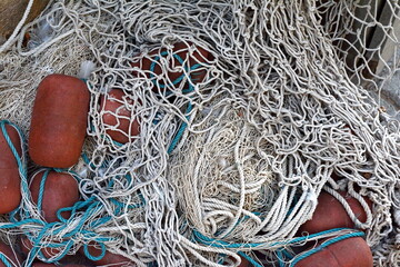 Detail of a pile of fishing nets with floating buoys. Detail of a big pile of white fishing nets with brown floating buoys and yellow ropes. Illuminated by sunlight.