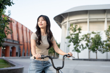 Pretty asian woman holding handle while riding on rental bicycle on pavement in park or city plaza.