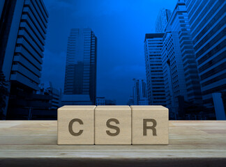 CSR acronym letter on wood block cubes on wooden table over modern office city tower and skyscraper, Corporate Social Responsibility concept
