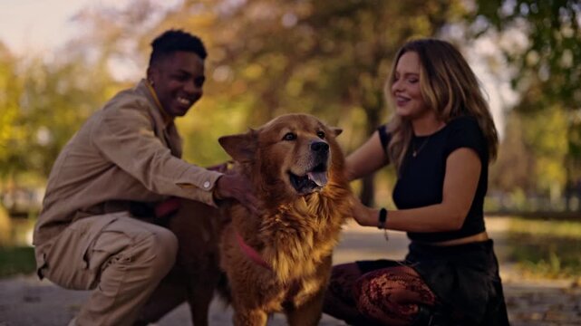 A cheerful young couple enjoys a walk in the park, stopping to lovingly pet their large, fluffy dog. Their smiles reflect the joy and affection they share with their beloved pet on a warm autumn day.