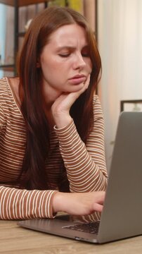 Young woman at home sits at laptop leans on hand looks sad tired and lacks motivation to work. Caucasian girl at desk faces severe burnout stares blank sighs feels fatigue and struggles with task list